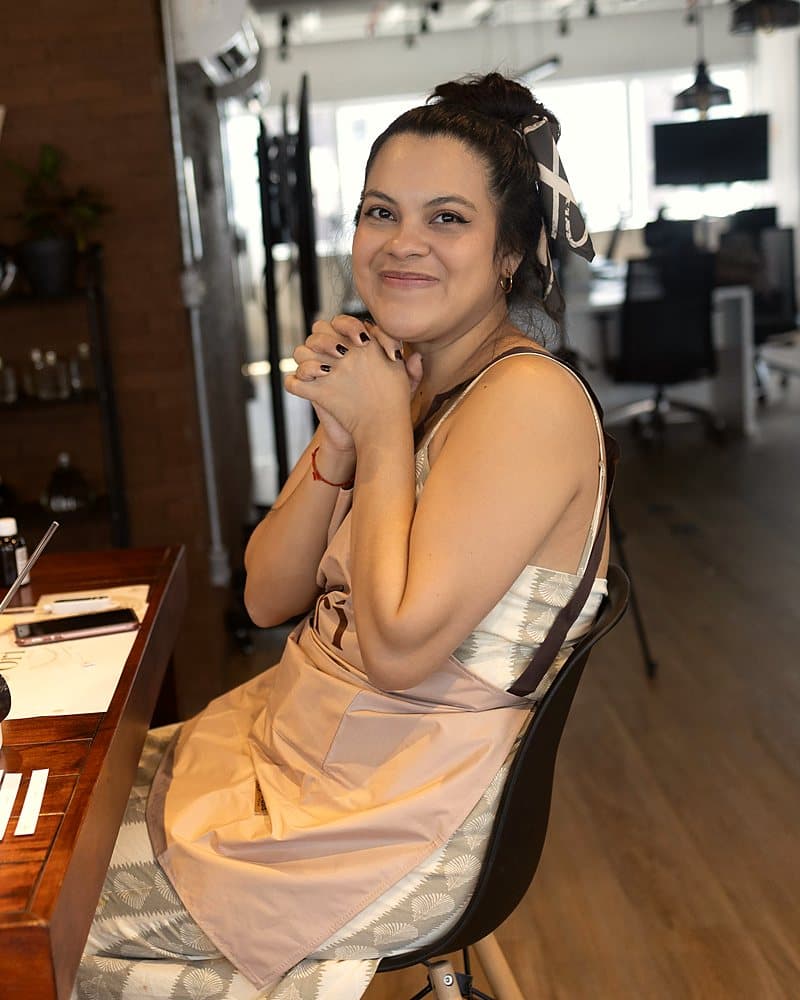 Participante sorrindo de avental, ao lado da própria bancada